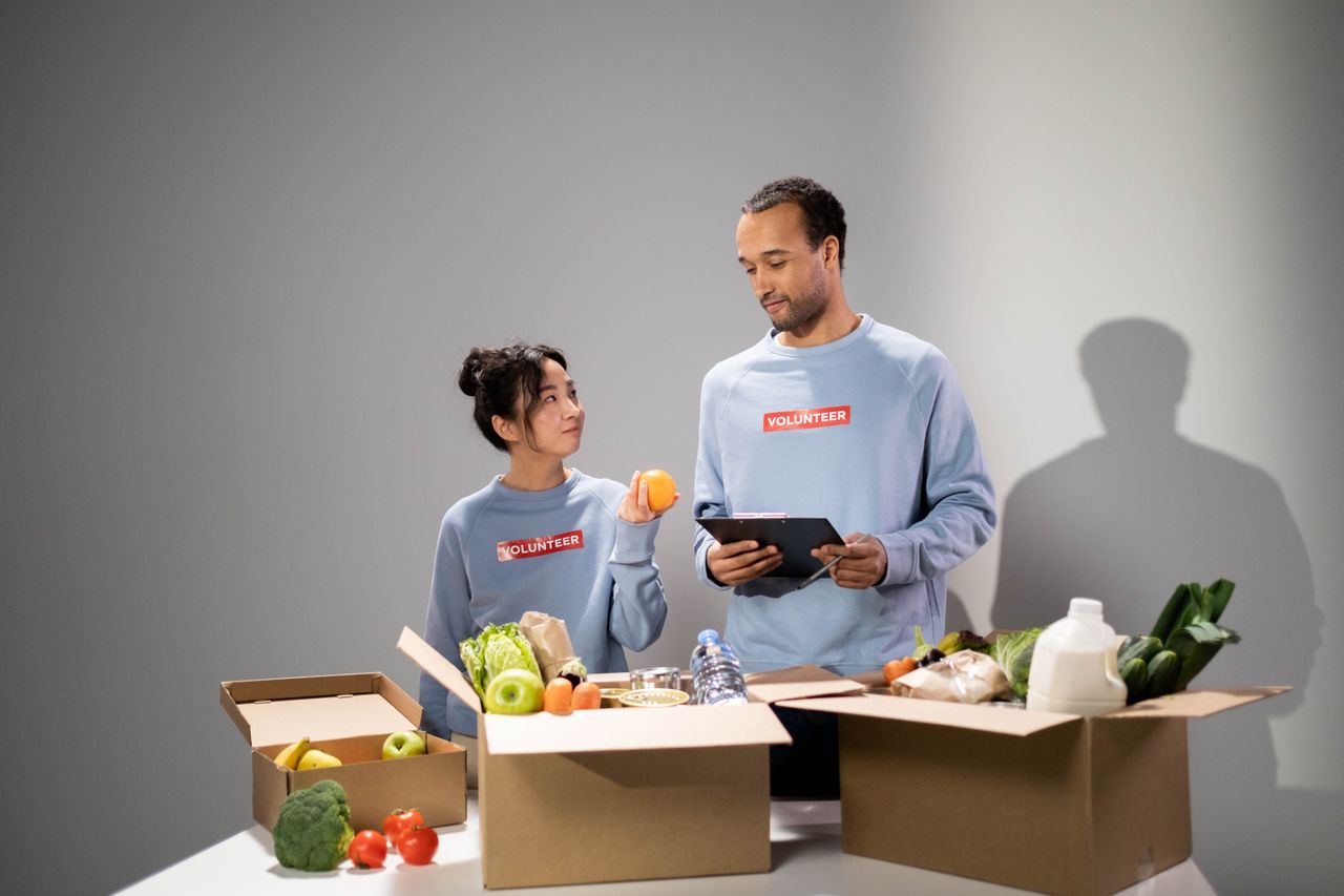 Two volunteers organize food items into boxes for community service indoors.