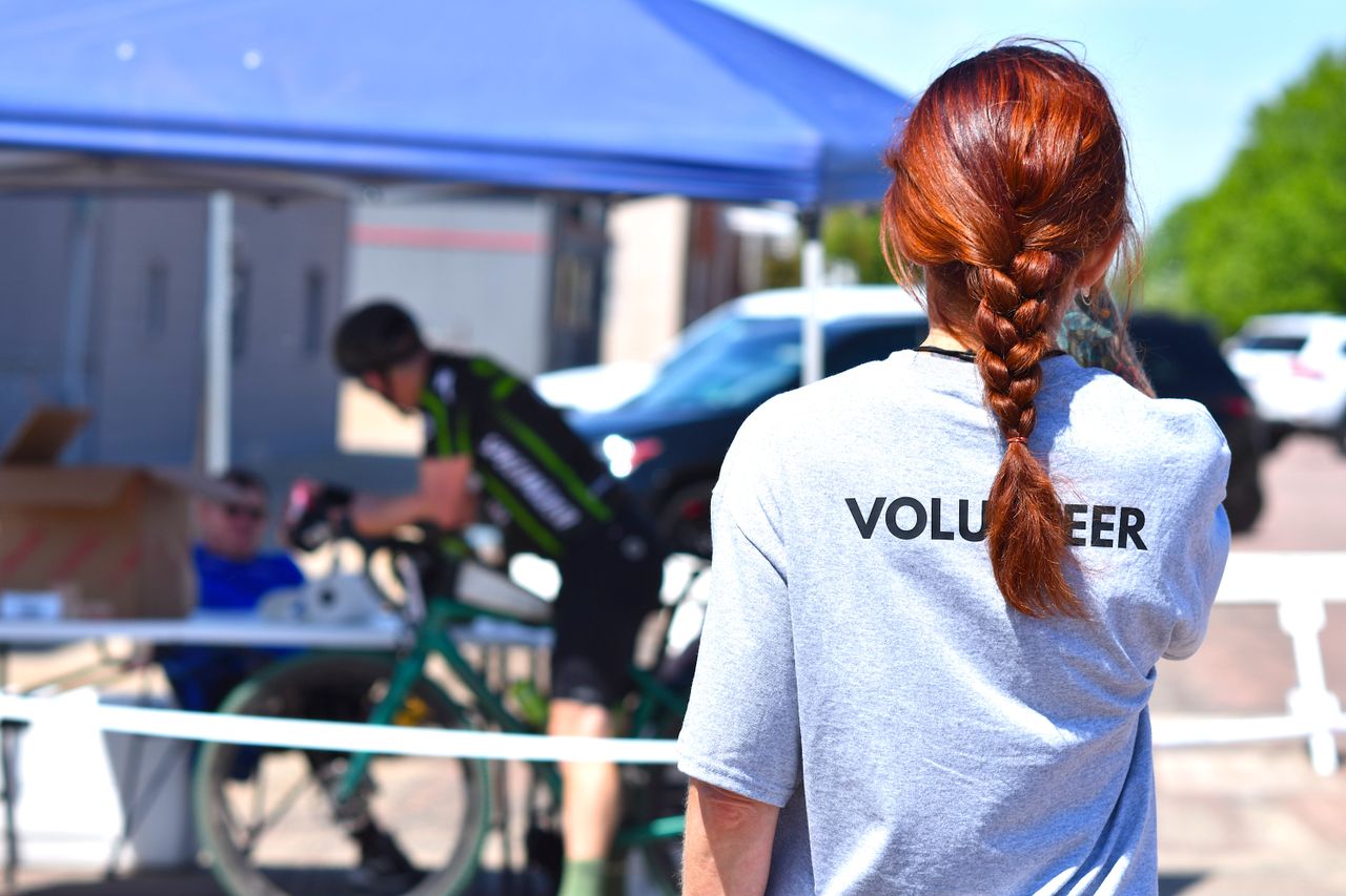 ours-journey A volunteer oversees a charity bike event under a blue tent on a sunny day.
